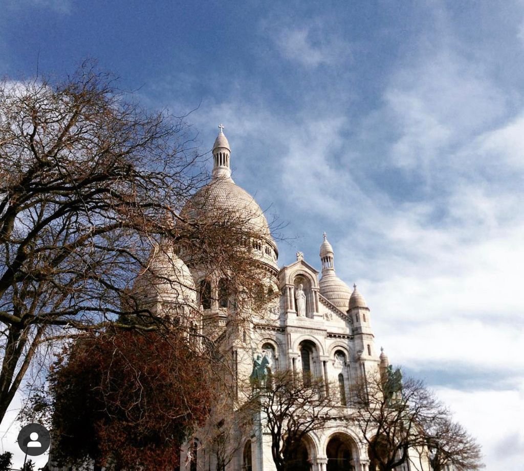 Stunning view of Sacre Coeur Basilica in Paris, framed by trees under a clear blue sky.